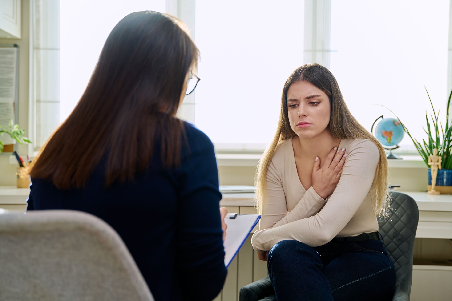 Sad unhappy young woman at therapy with female professional psychologist
